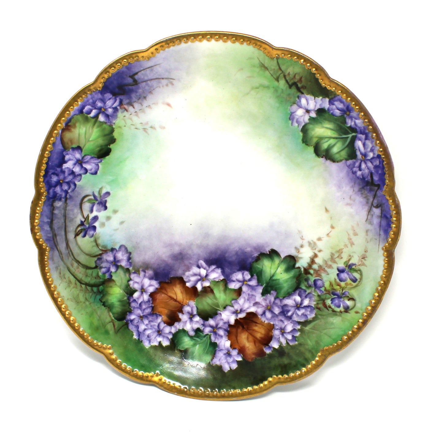 An antique scalloped Limoges France porcelain plate with a hand-painted floral design featuring purple flowers, green & brown leaves, and a gold moriage rim.