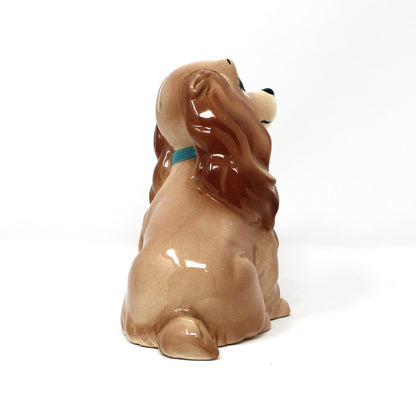 Side view of a vintage Hagen-Renaker ceramic coin bank.  Disney's "Lady" from the Movie, Lady and the Tramp. Cocker Spaniel dog wearing a small blue and yellow collar.