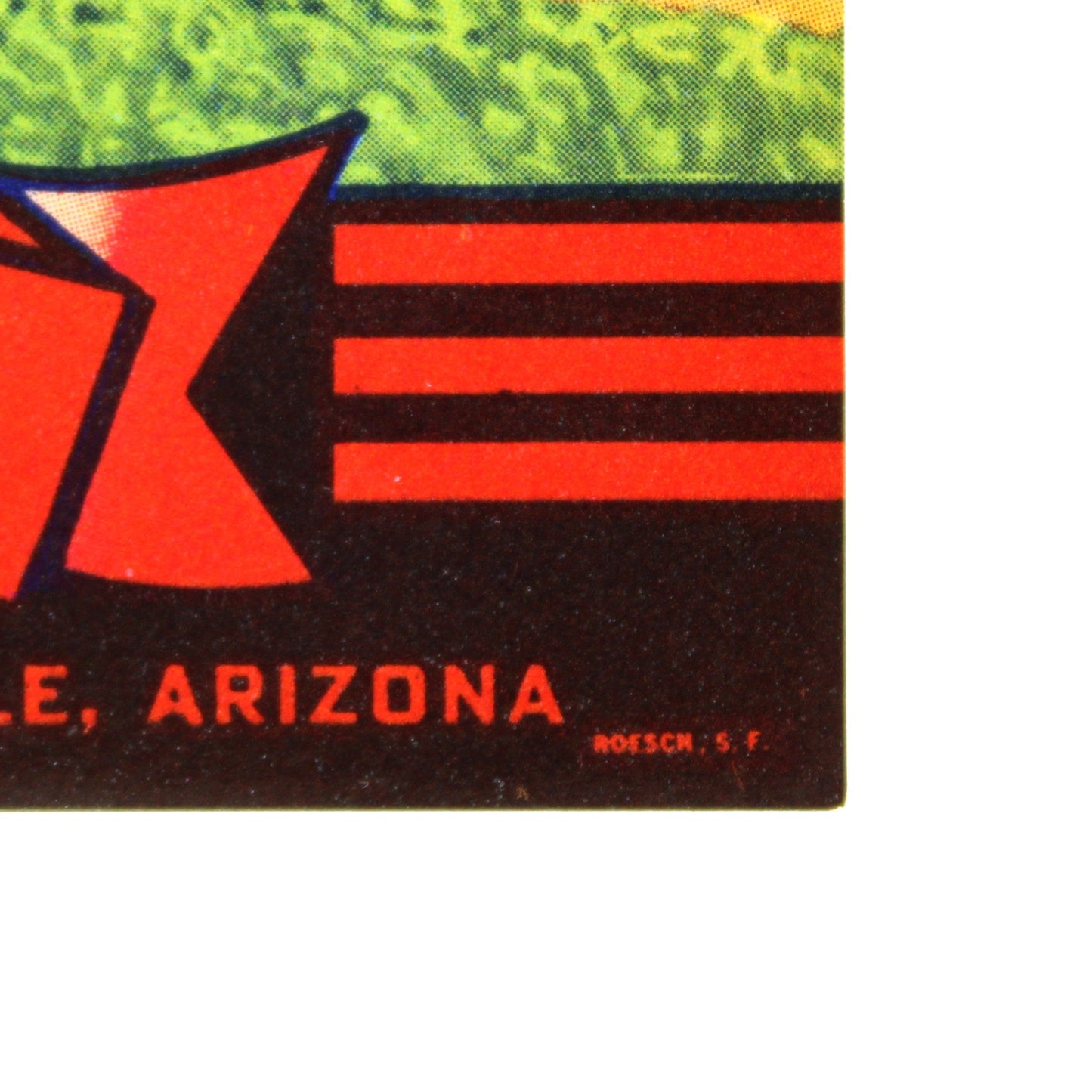 A close-up of a vintage-style printed label or package design showing a farm landscape with green fields, red-roofed buildings, and bold red, white, black, and yellow text including 'BLES' and 'Glendale, Arizona.'.