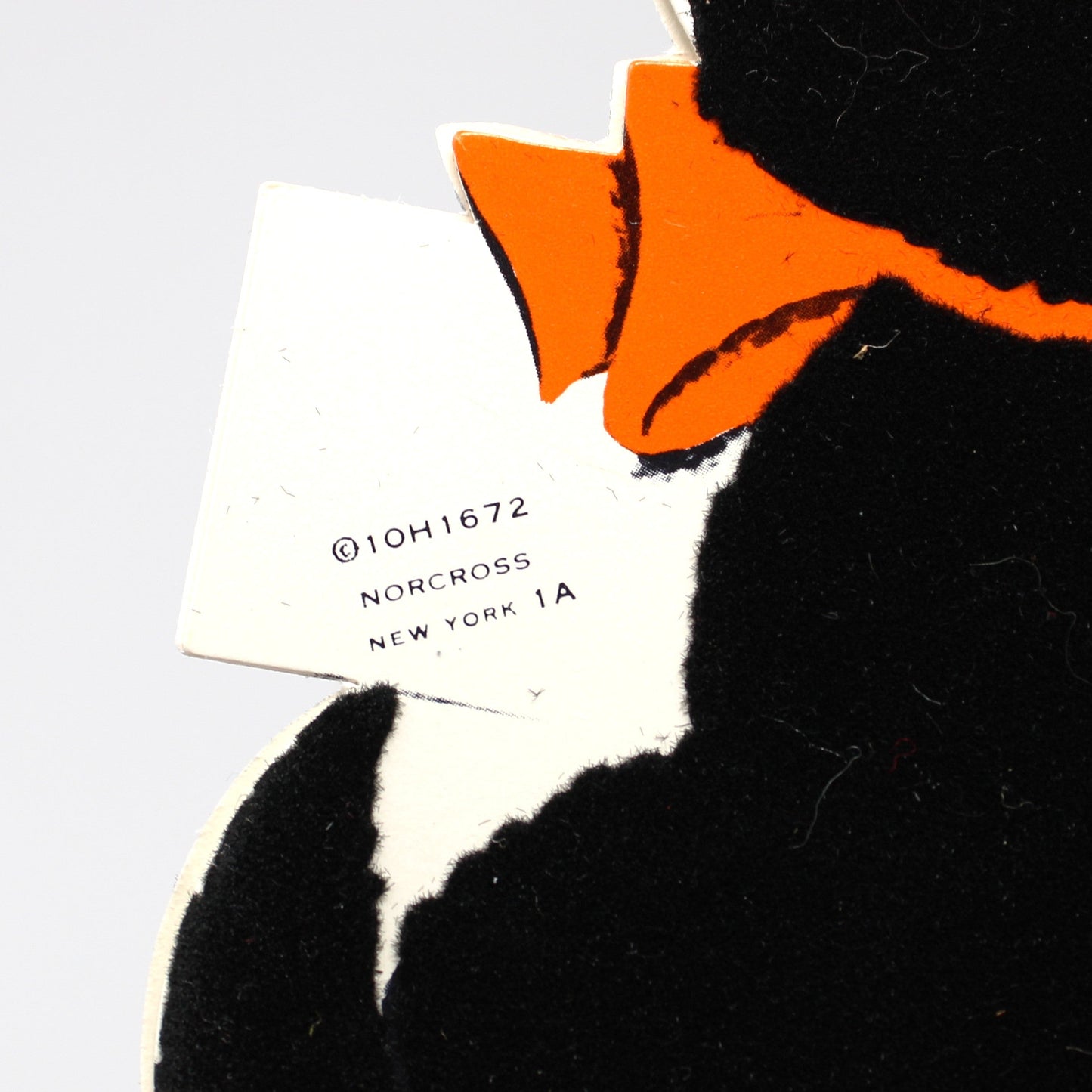 A close-up of a vintage Halloween card, a black plush flocked cat with a bright orange bow tie. Norcross.