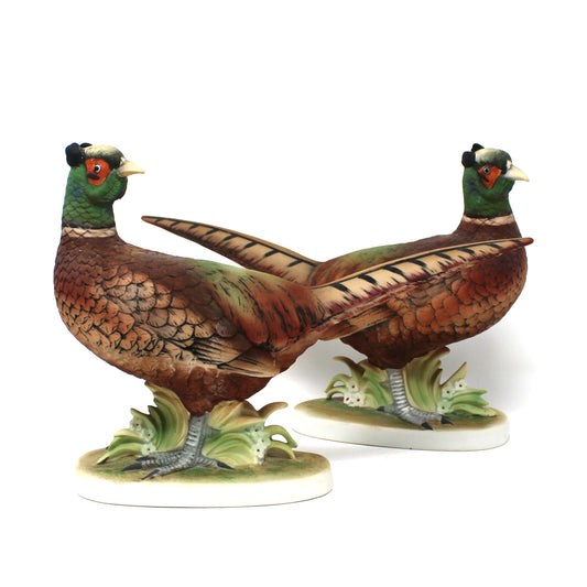 A pair of vintage pheasant figurines. The detailed hand-painted porcelain birds feature brown bodies, green necks, and red facial accents, standing on small leafy bases.