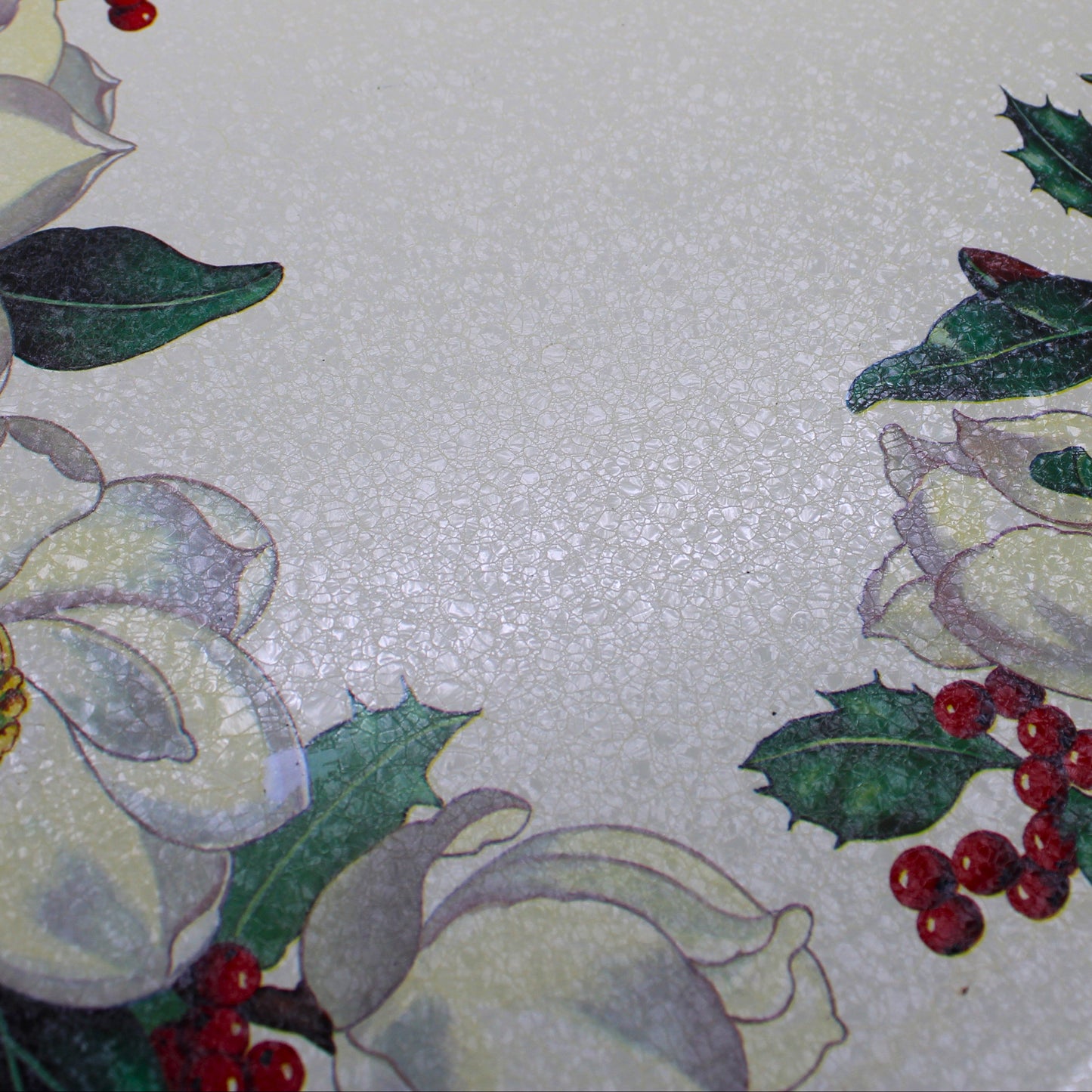 close up of texture from A vintage rectangular Christmas serving tray by Potpourri, with a cream-colored background, decorated with a border of white magnolia flowers, green holly leaves, and red berries.
