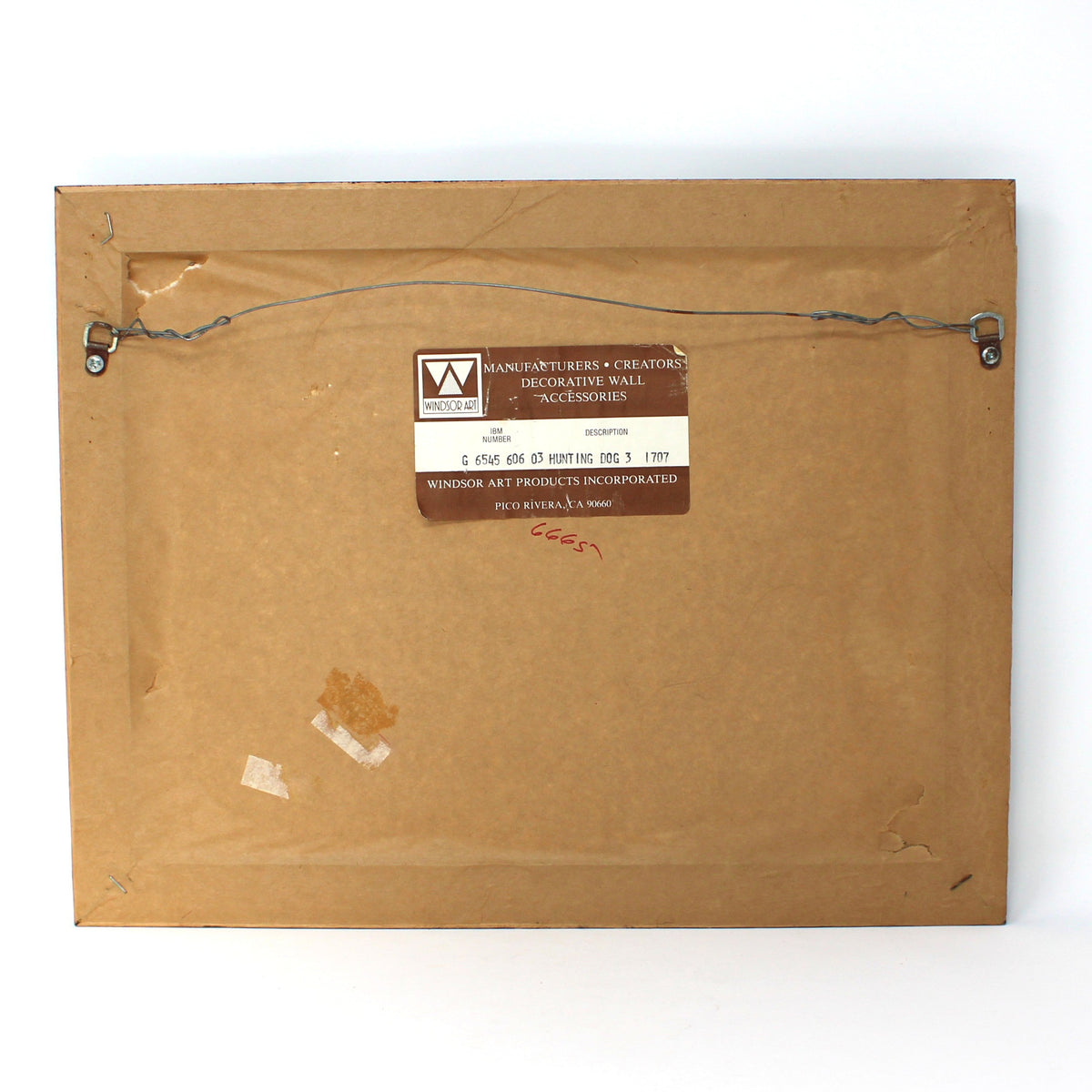 The back of a square brown cardboard picture frame with a wire hanger and a small label, photographed against a white studio backdrop.