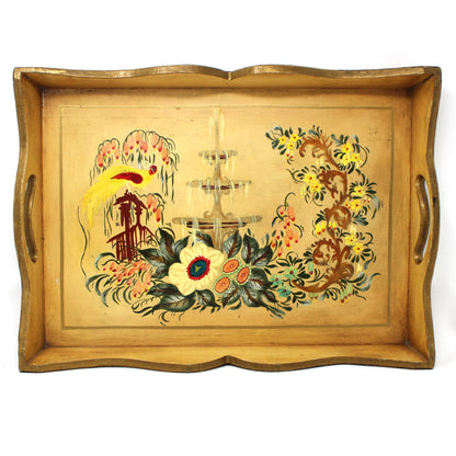 A rectangular vintage wooden serving tray with scalloped edges and two side handles, featuring a hand-painted floral and fountain garden design in warm tones on a light wood base.