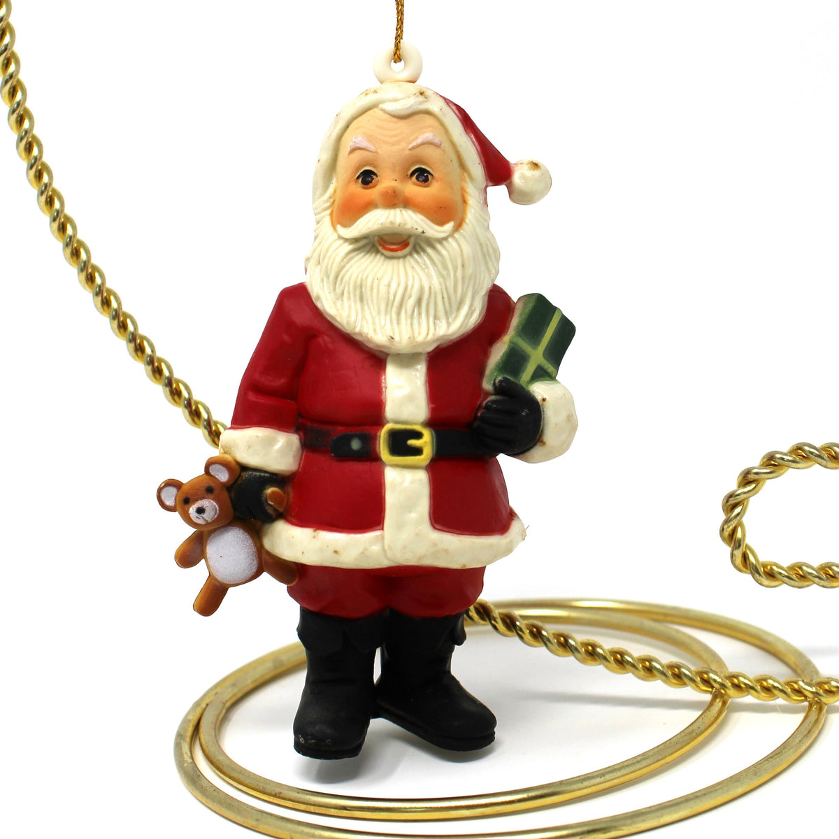 A vintage Santa Claus Christmas ornament with a gold hanging loop, featuring Santa in a red suit with white trim, holding a green gift box and a small brown teddy bear.  1970's Hong Kong, NOS.