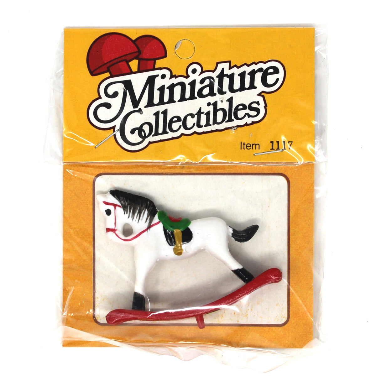 A miniature collectible rocking horse toy in its original packaging. The white plastic toy horse features black and red details, a green saddle, and rests on a red rocking base, all sealed inside a clear plastic bag with a yellow 'Miniature Collectibles' header card.