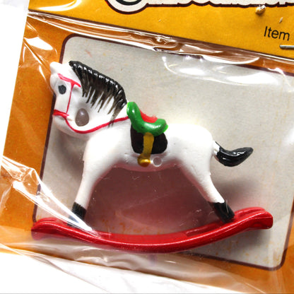 A miniature collectible rocking horse toy in its original packaging. The white plastic toy horse features black and red details, a green saddle, and rests on a red rocking base, all sealed inside a clear plastic bag with a yellow 'Miniature Collectibles' header card.