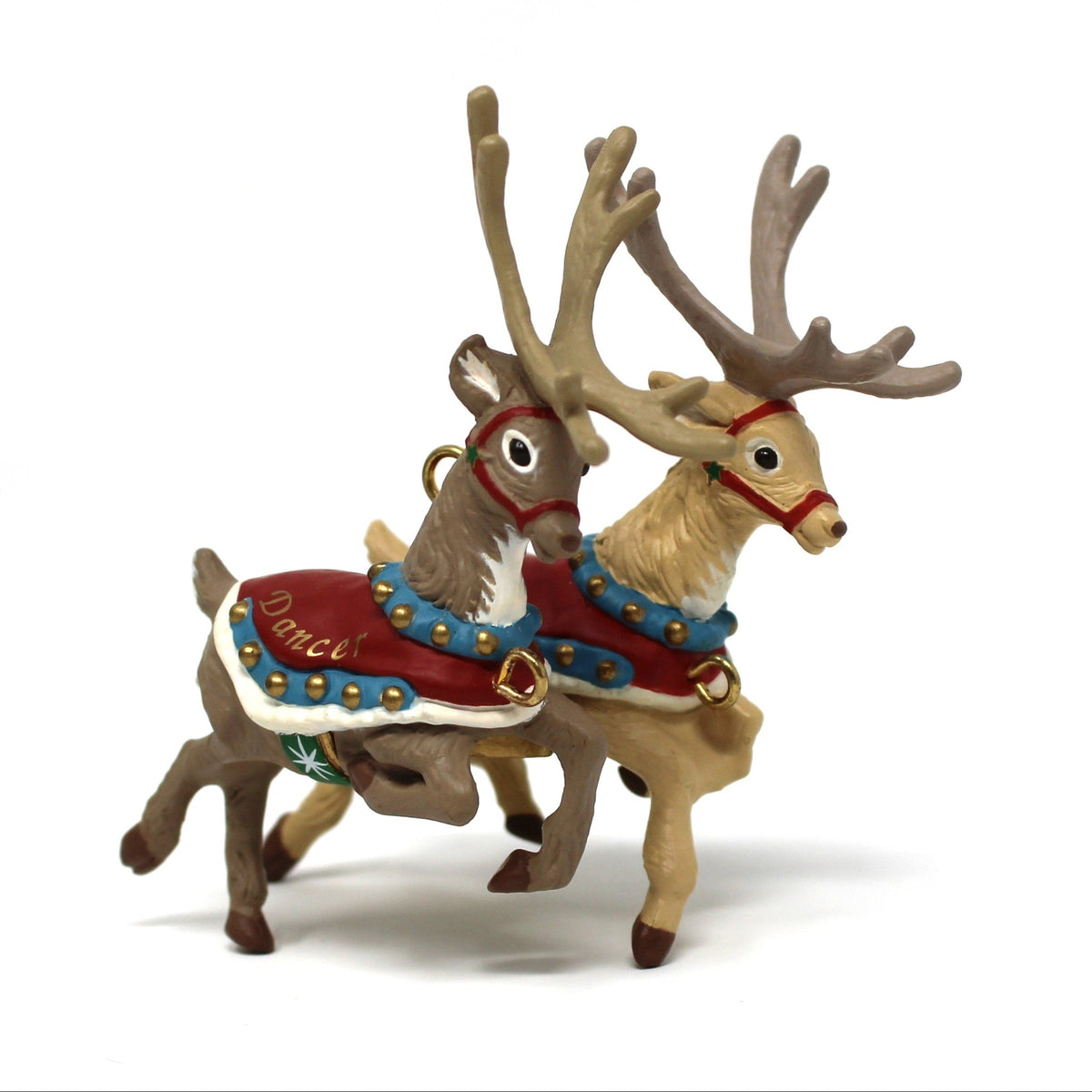 A vintage ornament figurine of two reindeer, one with antlers, wearing red and blue patterned harnesses, centered on a plain white background.