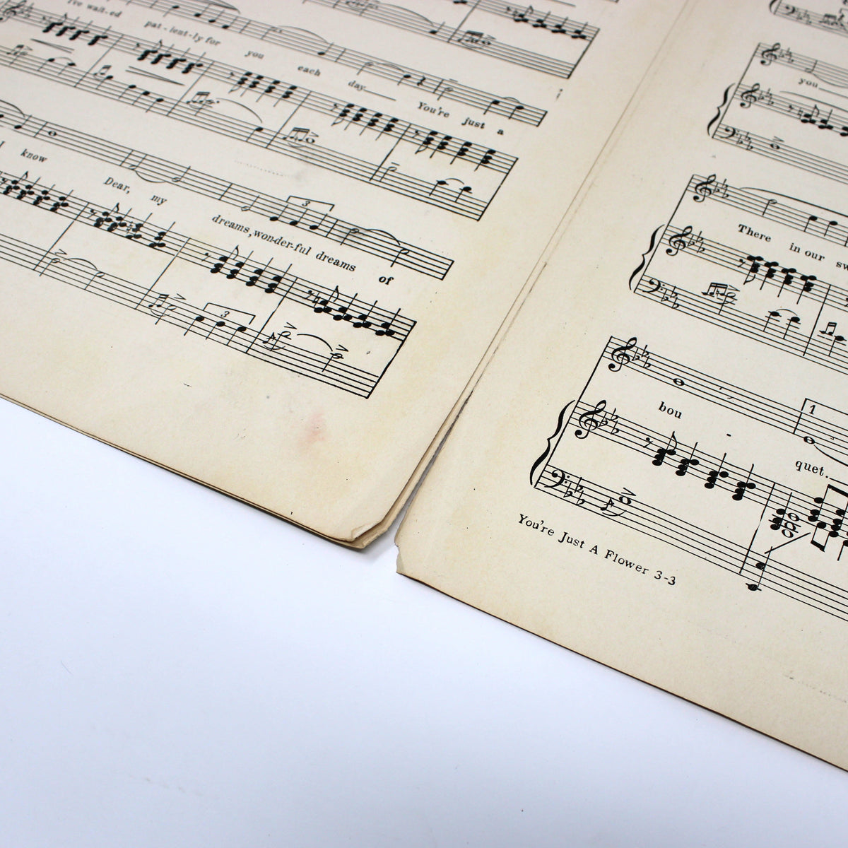 An open vintage sheet music book showing printed musical staves and notes on aged cream-colored paper, photographed on a white surface.