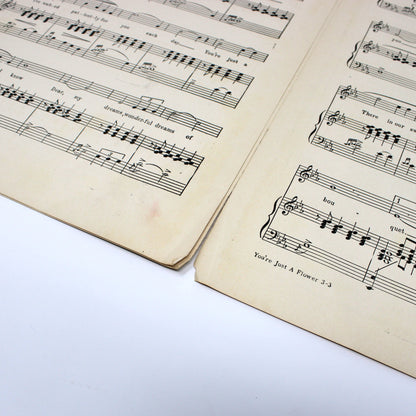 An open vintage sheet music book showing printed musical staves and notes on aged cream-colored paper, photographed on a white surface.