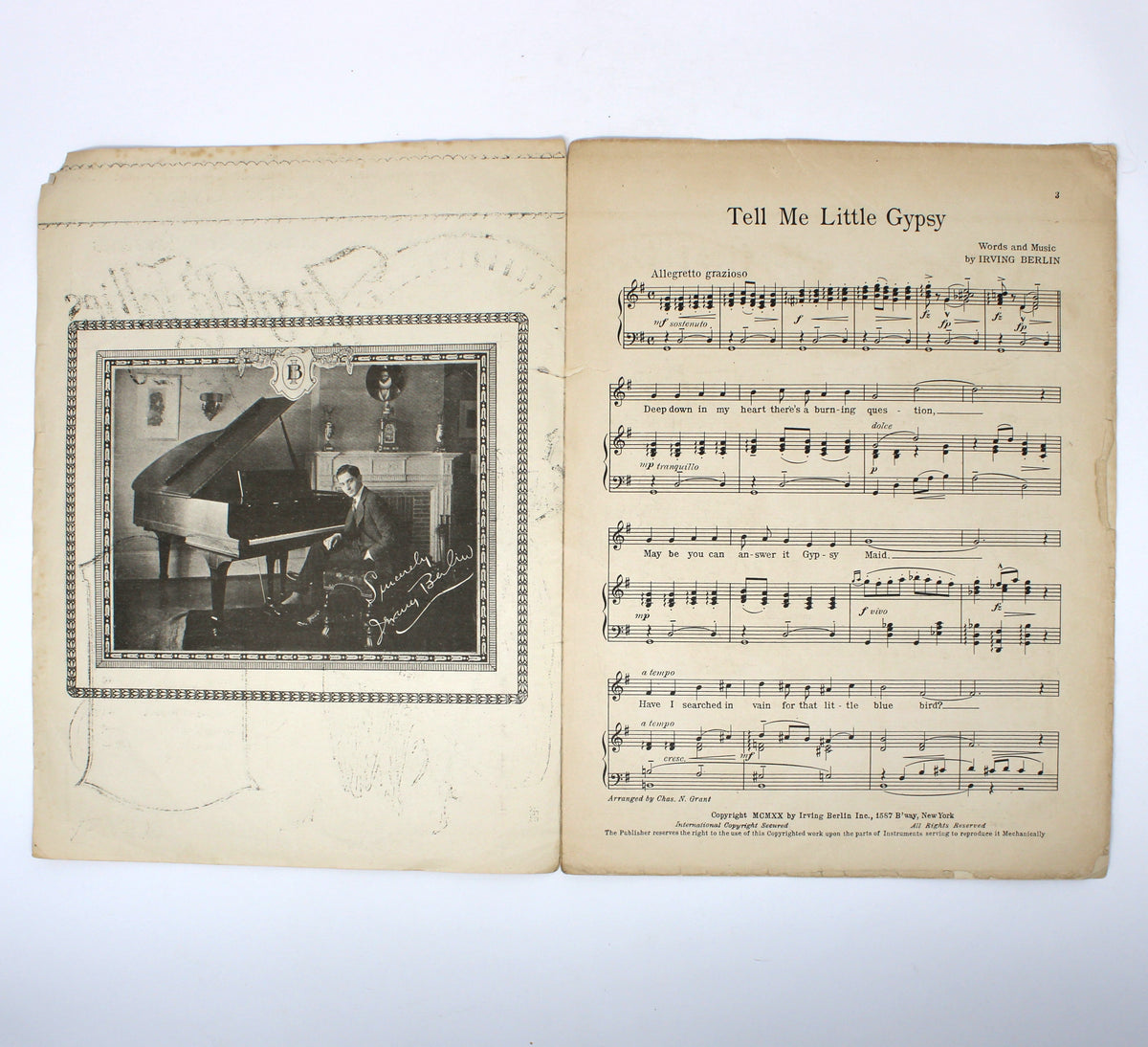 An open vintage music book or program on a white surface, showing an aged yellowed page with a black-and-white illustration of a person playing a grand piano on the left and sheet music titled 'Tell Me Little Gypsy' on the right.
