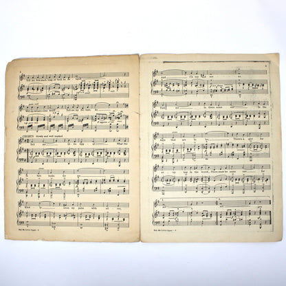 An open vintage music book showing two pages of printed sheet music with aged yellowed paper and black musical notation, photographed against a plain white background.