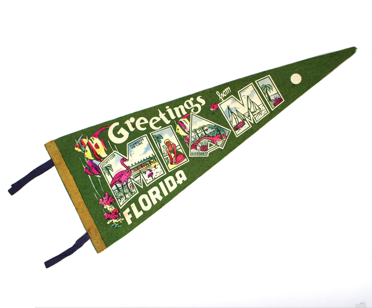 A vintage green triangular pennant flag with 'Greetings from Miami Florida' printed across it, featuring colorful illustrated panels and two dark blue ties, shown on a plain white background.