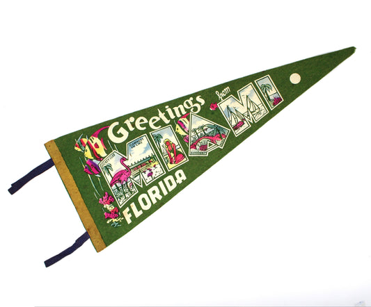 A vintage green triangular pennant flag with 'Greetings from Miami Florida' printed across it, featuring colorful illustrated panels and two dark blue ties, shown on a plain white background.