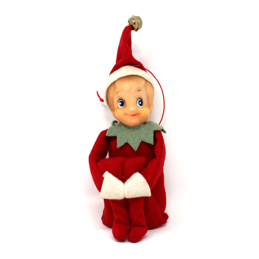 A small plush Christmas elf doll wearing a red outfit and pointed red hat with white trim, seated against a plain white background.