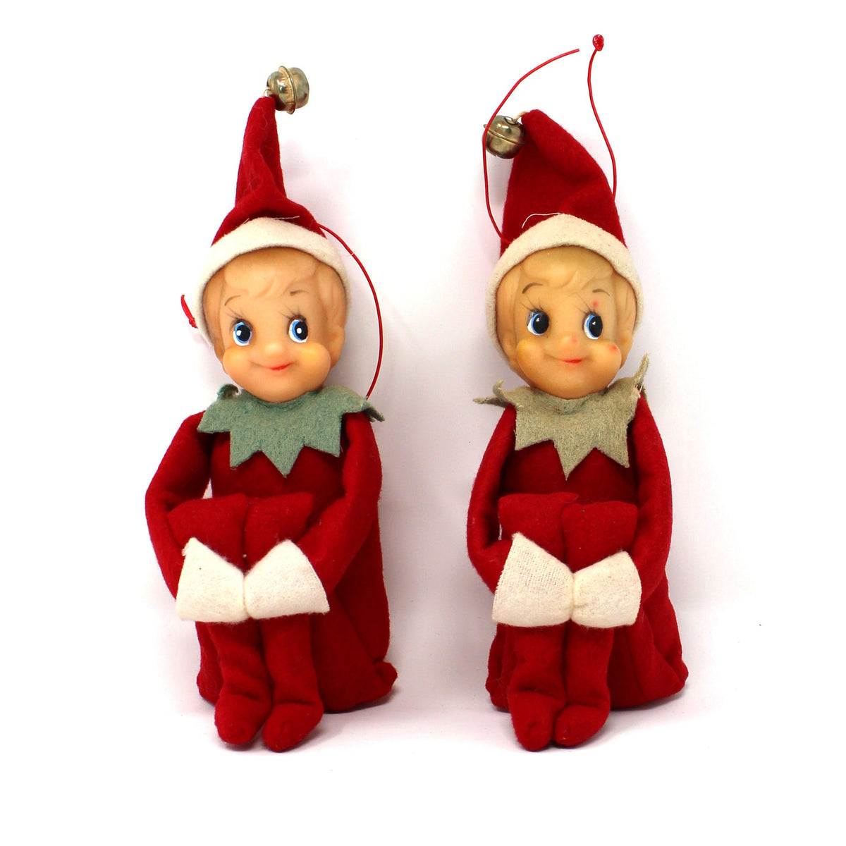 Two small elf-shaped ornaments in red and white clothing with green collars, standing side by side on a plain white background.