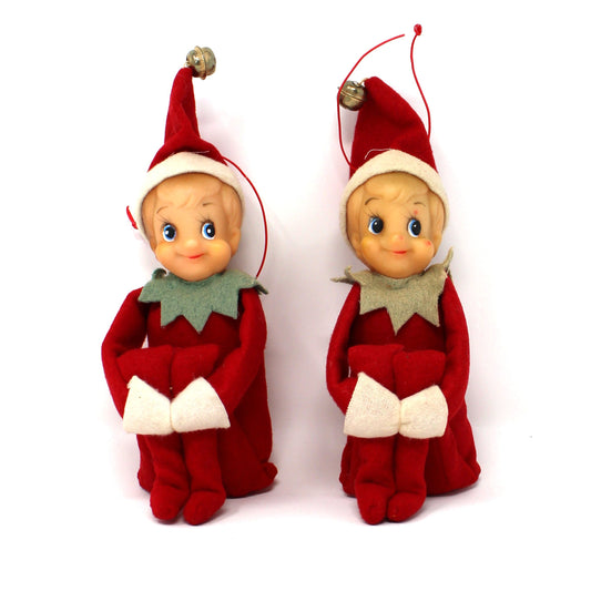 Two small elf-shaped ornaments in red and white clothing with green collars, standing side by side on a plain white background.