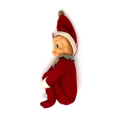 A small elf-shaped ornament or figurine wearing a red outfit with a white-trimmed hat and a light green neck scarf, shown against a plain white background.