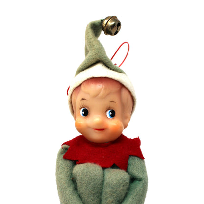 Vintage Christmas elf ornament featuring a plastic face, green felt clothing, a red felt collar, and a green pointed hat with a gold bell, shown against a plain white background.