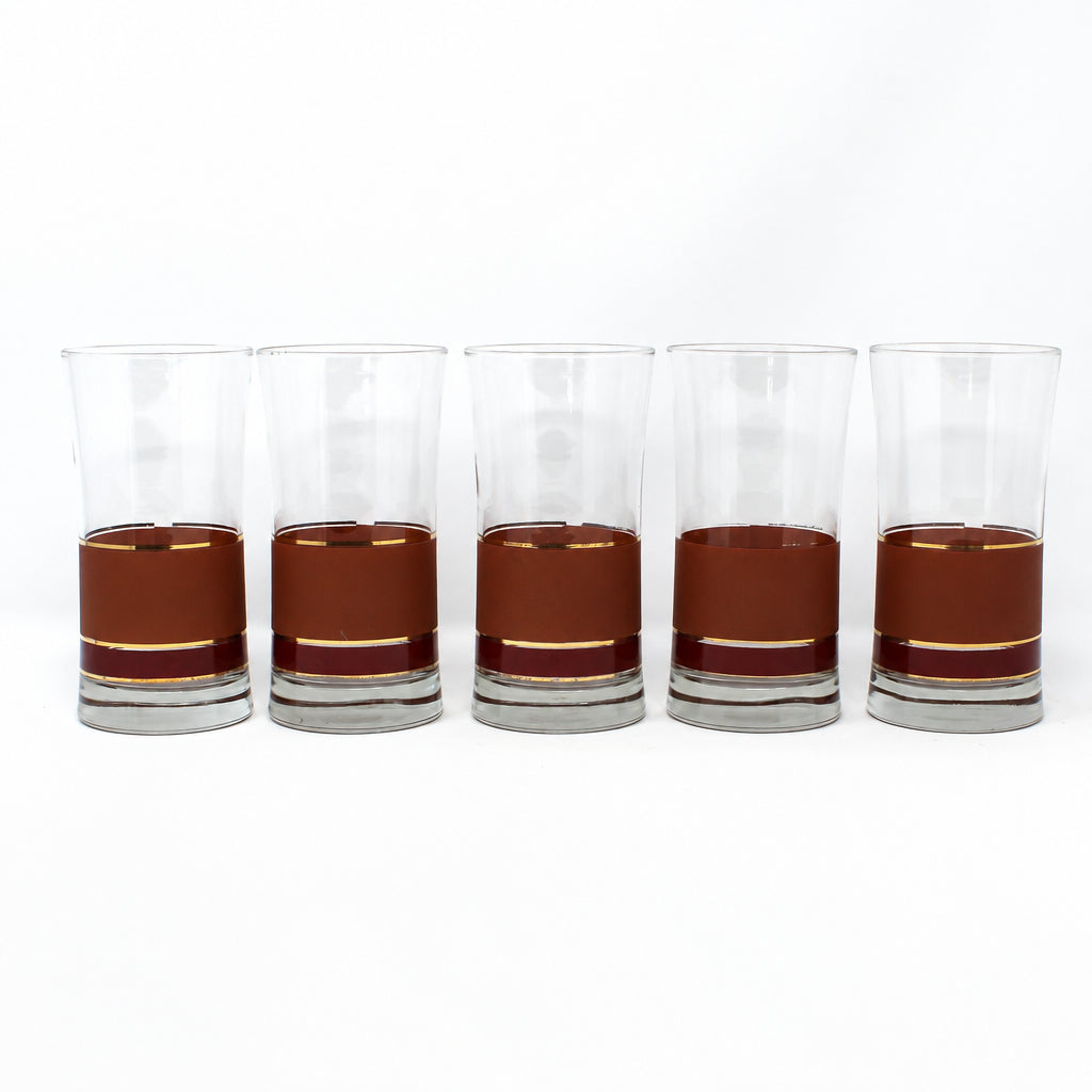 Five clear lowball glasses filled with a brown liquid, arranged in a row on a white studio background.