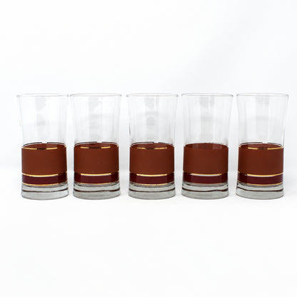 Five clear lowball glasses filled with a brown liquid, arranged in a row on a white studio background.
