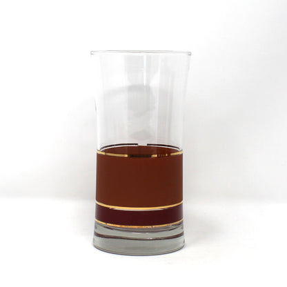 A clear glass tumbler with a flared rim, partially filled with a dark amber-brown liquid, set against a plain white background.