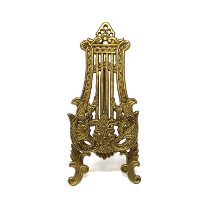 A vintage, ornate brass tabletop display stand / easel, resembling a gothic or baroque-style lyre or harp.