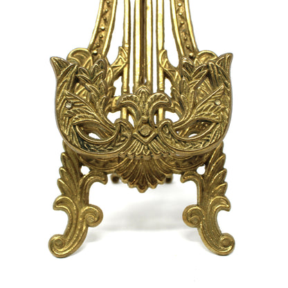 An ornate brass-colored metal stand with intricate scrollwork and decorative  details.