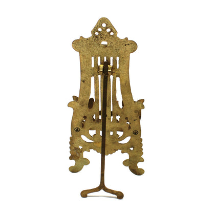 An ornate vintage brass stand with intricate cutout details and a three-legged base