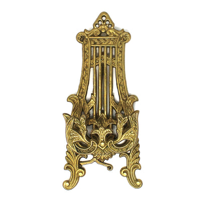 A vintage ornate brass tabletop easel / display stand with intricate scrollwork and vertical bar details, shown closed.