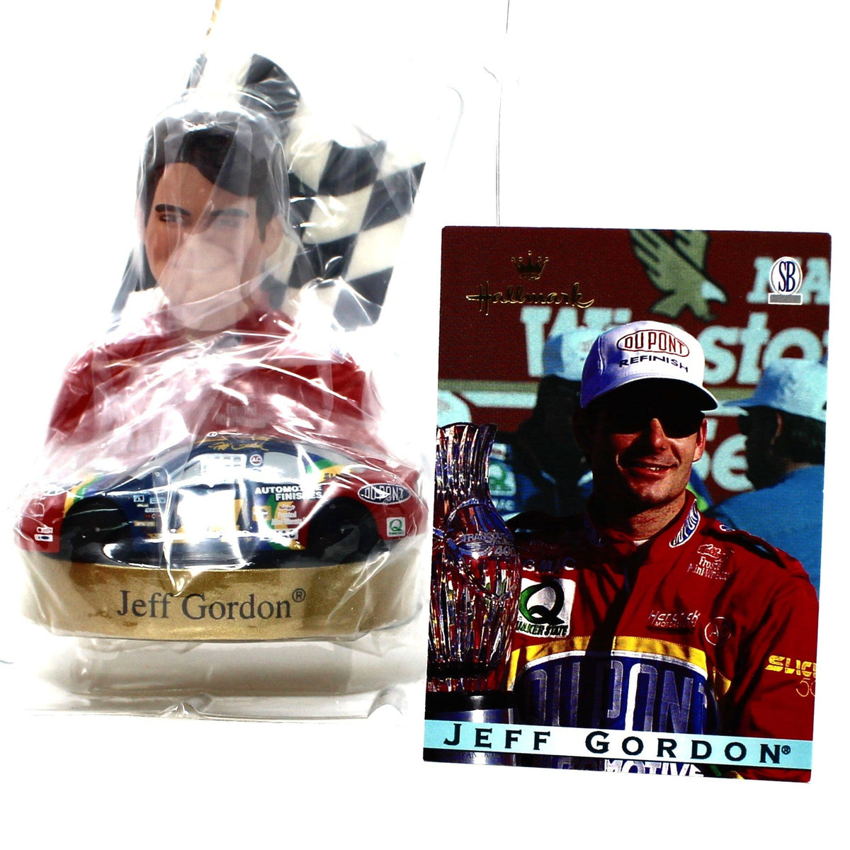 A NASCAR-themed ornament featuring Jeff Gordon in a red racing suit with a checkered flag and gold car base, shown next to a printed collectible trade card with the same driver's image 