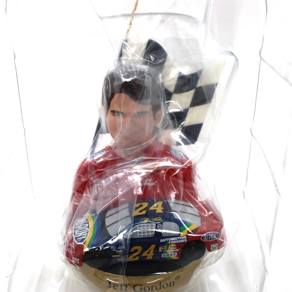 A Jeff Gordon NASCAR collectible Christmas ornament inside its original clear plastic packaging, wearing a red racing suit with the number 24.