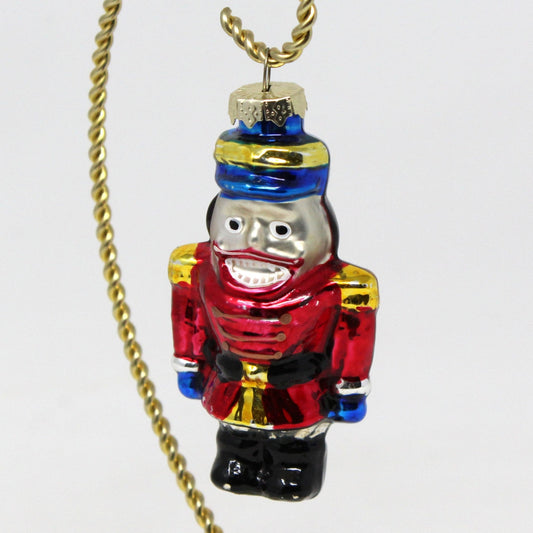 A vintage hand-painted glass nutcracker ornament.   Nutcracker soldier in red, blue, black, gold, and silver colors.