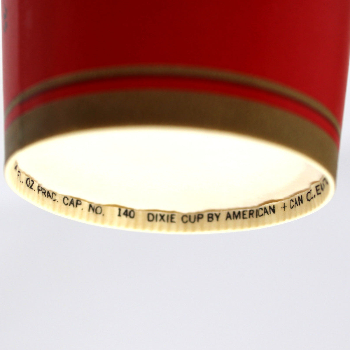 A close-up of a red Dixie cup with a gold band and printed black text on the rim, shown against a plain white background.
