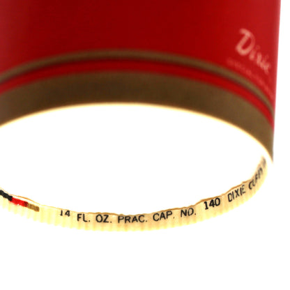 A close-up of a red vintage paper cup with printed text reading '14 FL OZ PRAC CAP NO. 140, Dixie Cups