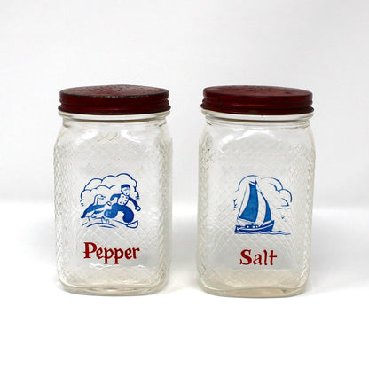 A set of vintage clear glass salt and pepper shakers from Hazel Atlas. Featuring a blue blue sailboat and a Dutch boy, plus the word word 'Pepper' or 'Salt' printed in red below the illustration.