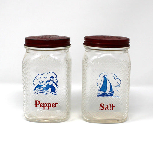 A set of vintage clear glass salt and pepper shakers from Hazel Atlas. Featuring a blue blue sailboat and a Dutch boy, plus the word word 'Pepper' or 'Salt' printed in red below the illustration.
