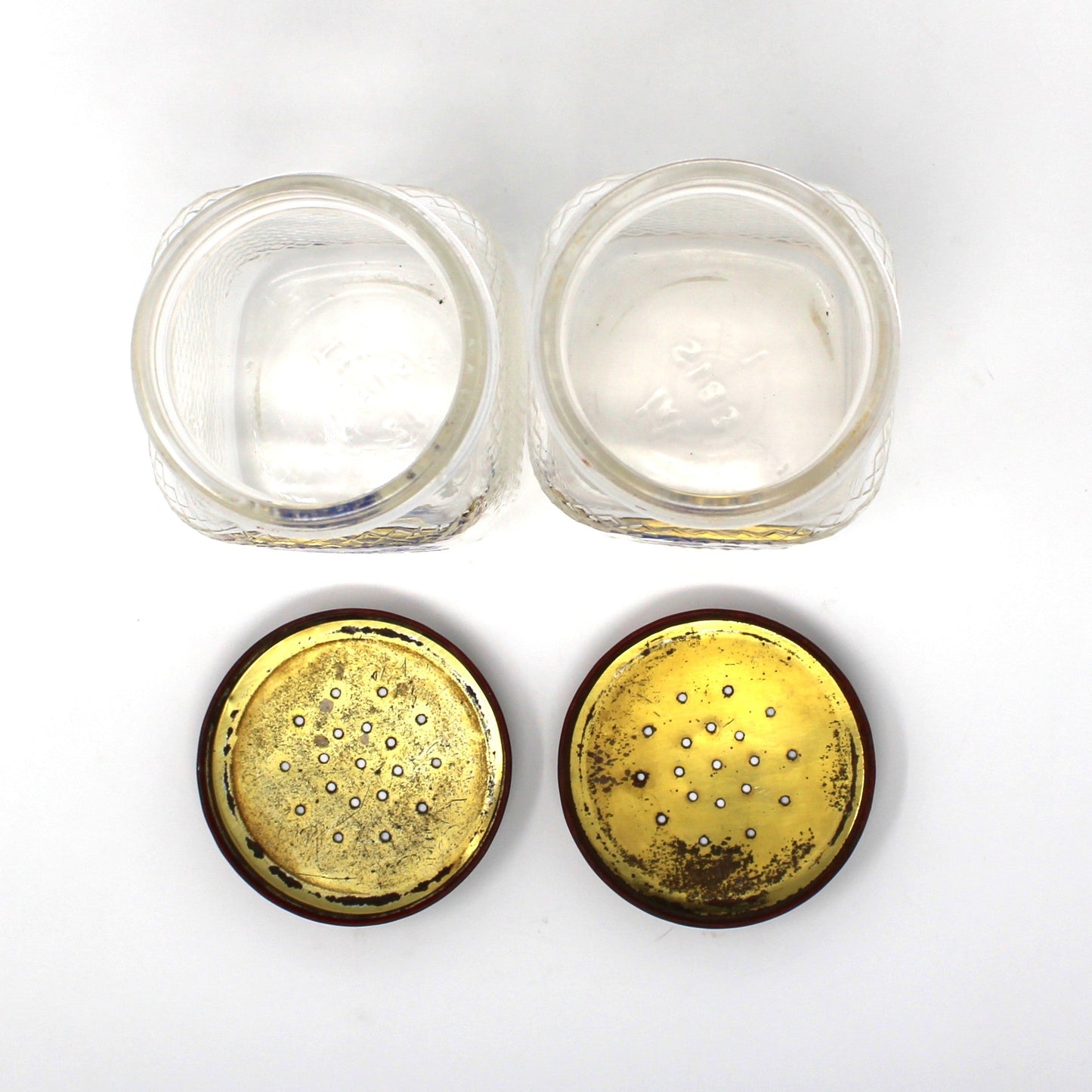 View of vintage salt and pepper glass jars opened plus their lids turned upside down to show the inside.  