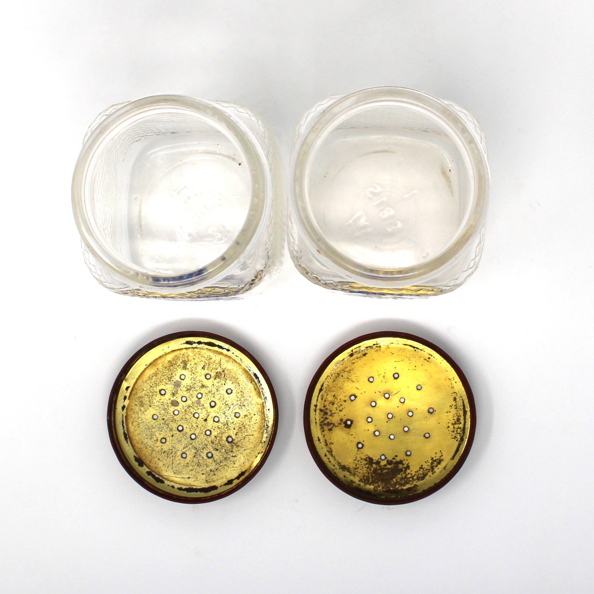 View of vintage salt and pepper glass jars opened plus their lids turned upside down to show the inside.  