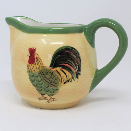 A Pfaltzgraff Napoli stoneware creamer with a green rim and handle, featuring a hand-painted rooster design in the center.